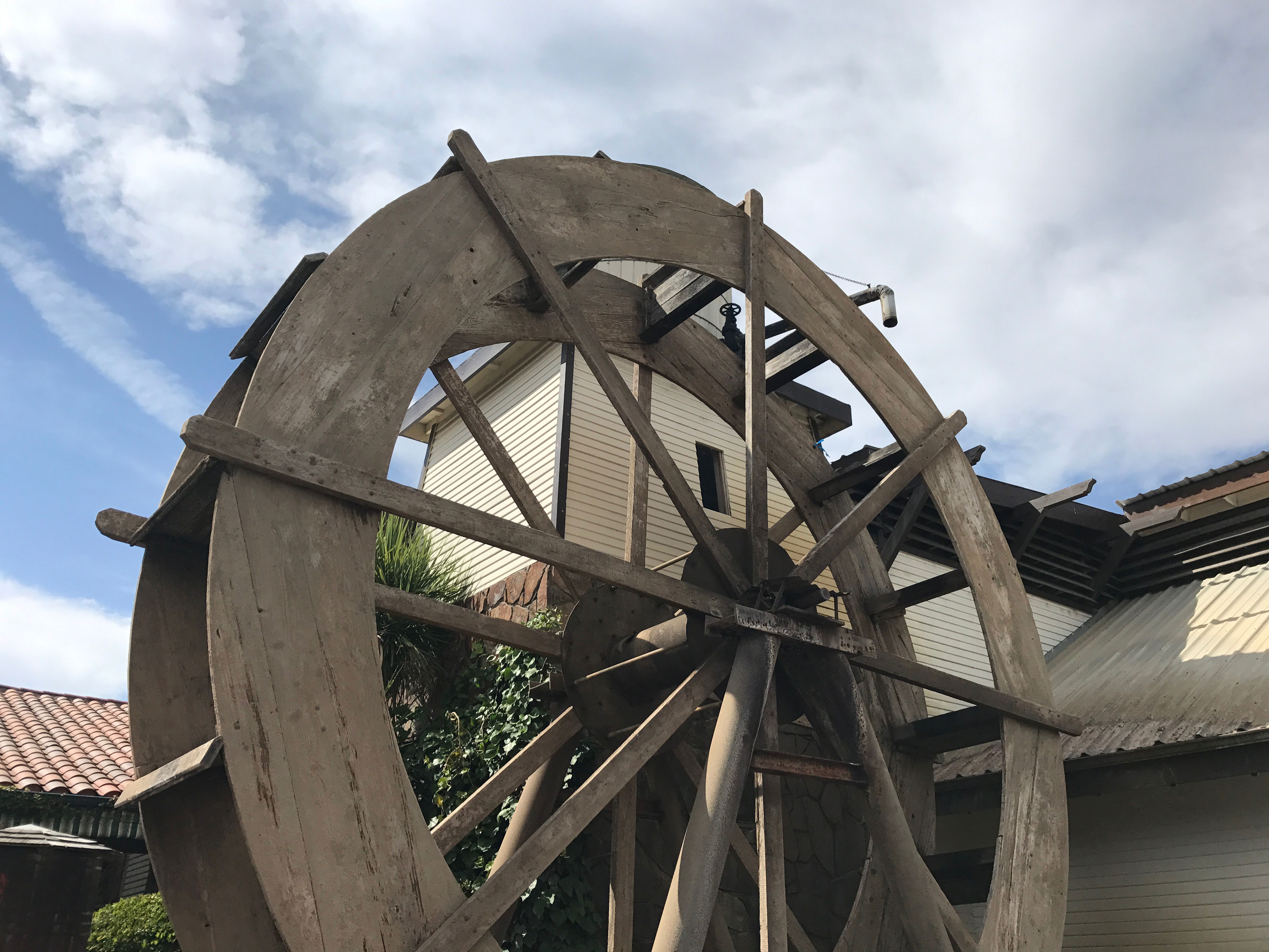 A photo looking up at a water wheel and its surrounding building, with the sky and clouds above.